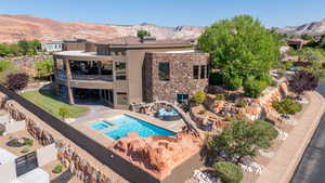 Rear view of house with a mountain view, stucco siding, a balcony, a pool with connected hot tub, and stone siding