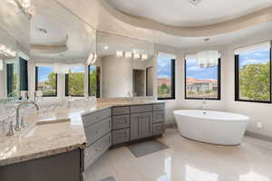 Bathroom featuring a raised ceiling, a chandelier, double vanity, a soaking tub, and tile patterned flooring
