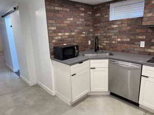 Kitchen featuring finished concrete floors, stainless steel dishwasher, black microwave, white cabinetry, and dark countertops