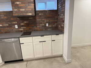 Kitchen featuring finished concrete floors, stainless steel dishwasher, dark countertops, and white cabinetry