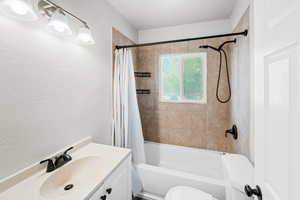 Full bathroom with shower / bath combo with shower curtain, vanity, and a textured wall