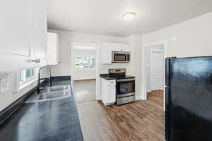 Kitchen with stainless steel appliances, wood finished floors, white cabinetry, and dark countertops