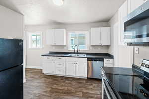 Kitchen featuring stainless steel appliances, dark countertops, white cabinetry, dark wood-style flooring, and a textured ceiling