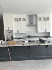Kitchen featuring white cabinets, wall chimney range hood, decorative backsplash, glass insert cabinets, and recessed lighting