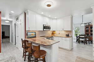 Kitchen with light stone countertops, a peninsula, white cabinetry, a breakfast bar area, and ceiling fan