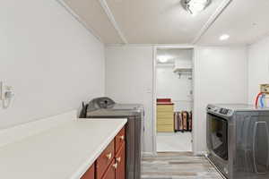 Washroom featuring washing machine and dryer, a textured ceiling, cabinet space, and light wood finished floors