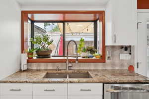Kitchen featuring dishwasher, light stone counters, decorative backsplash, and white cabinetry