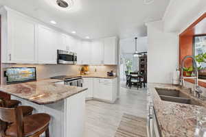 Kitchen featuring recessed lighting, a ceiling fan, white cabinets, a peninsula, and light stone counters