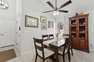 Dining room featuring light wood-style floors, ceiling fan, a chandelier, and high vaulted ceiling
