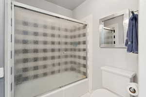 Bathroom featuring bath / shower combo with glass door and toilet