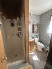 Bathroom with a textured ceiling, a stall shower, vanity, and wallpapered walls