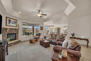 Living room featuring a tray ceiling, ceiling fan, a chandelier, a fireplace, and carpet floors