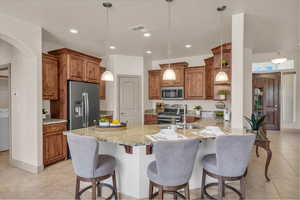 Kitchen with light tile patterned floors, brown cabinets, a peninsula, stainless steel appliances, and light stone counters