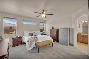 Bedroom featuring light carpet, arched walkways, connected bathroom, and ceiling fan