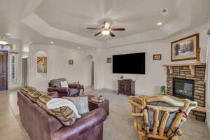 Living area with arched walkways, recessed lighting, a raised ceiling, a ceiling fan, and a stone fireplace