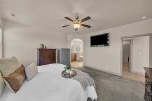Bedroom featuring light colored carpet, arched walkways, light tile patterned flooring, ensuite bath, and ceiling fan