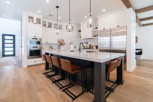 Kitchen featuring open shelves, light countertops, light wood-type flooring, a breakfast bar, and beam ceiling