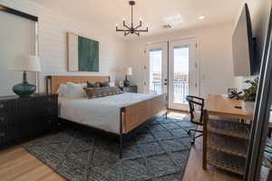 Bedroom with access to exterior, french doors, wood finished floors, a chandelier, and wood walls