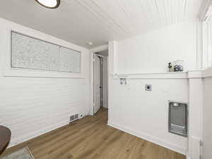 Laundry area with hookup for an electric dryer, light wood-style flooring, hookup for a washing machine, brick wall, and wooden ceiling