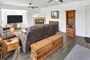 Living area with ceiling fan, dark wood-style floors, and a fireplace