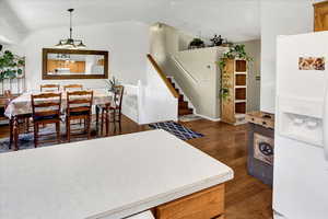 Kitchen with white refrigerator with ice dispenser, vaulted ceiling, dark wood finished floors, light countertops, and hanging light fixtures