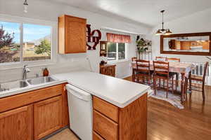 Kitchen with a peninsula, white dishwasher, light countertops, light wood-type flooring, and lofted ceiling