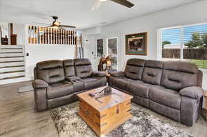 Living room featuring a ceiling fan, light wood finished floors, and stairs