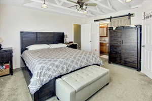 Bedroom with a barn door, carpet, beamed ceiling, a ceiling fan, and connected bathroom