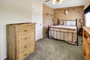 Carpeted bedroom featuring wood walls and ceiling fan