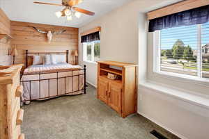 Bedroom with carpet floors, wood walls, and a ceiling fan