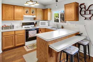 Kitchen featuring gas range, a peninsula, white microwave, light countertops, and a breakfast bar