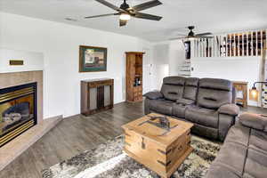 Living area featuring a ceiling fan, wood finished floors, a fireplace, and stairway