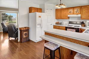 Kitchen featuring white appliances, light countertops, dark wood-style flooring, and brown cabinets