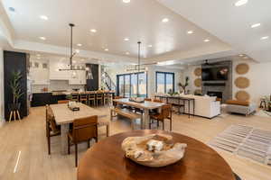 Dining space featuring a raised ceiling, a fireplace, light wood-style floors, recessed lighting, and ceiling fan