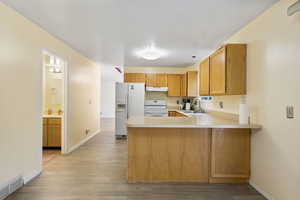 Kitchen featuring a peninsula, light countertops, white appliances, light wood-type flooring, and under cabinet range hood