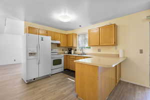 Kitchen featuring white appliances, a peninsula, light countertops, a textured ceiling, and light wood-style flooring