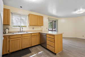 Kitchen with a peninsula, a textured ceiling, light wood-style floors, stainless steel dishwasher, and light countertops