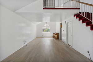 Unfurnished living room featuring a chandelier, wood finished floors, stairway, and vaulted ceiling
