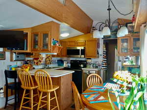Kitchen with lofted ceiling, light countertops, stainless steel appliances, a peninsula, and brown cabinets