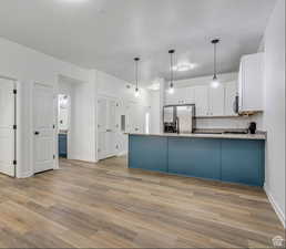 Kitchen featuring light wood finished floors, white cabinetry, stainless steel fridge, and a peninsula