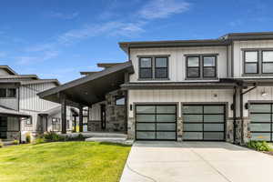 View of front of house featuring stone siding, a garage, concrete driveway, a front lawn, and board and batten siding