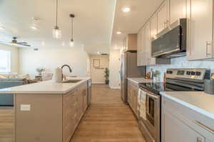 Kitchen featuring stainless steel appliances, open floor plan, light wood-style flooring, light countertops, and ceiling fan