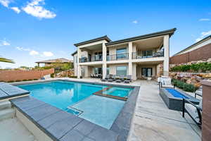 Back of house featuring a balcony, a patio area, stucco siding, a pool with connected hot tub, and french doors