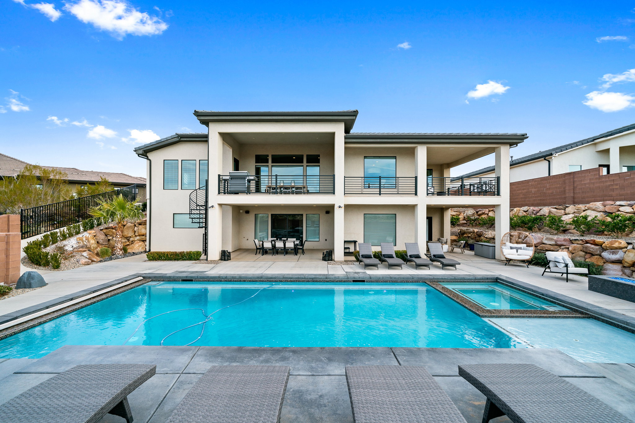 Back of property with a balcony, stucco siding, a patio area, a pool with connected hot tub, and stairs