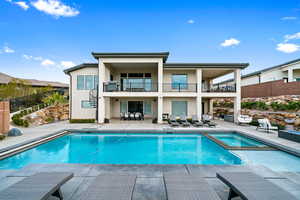 Back of property with a balcony, stucco siding, a patio area, a pool with connected hot tub, and stairs