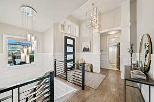 Foyer entrance with a decorative wall, wood-type flooring, a wainscoted wall, a chandelier, and a high ceiling