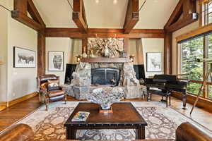 Living room featuring wood finished floors, a stone fireplace, beam ceiling, and high vaulted ceiling