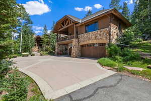 View of property exterior featuring concrete driveway, stone siding, an attached garage, roof with shingles, and a balcony