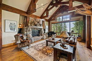 Living area with hardwood / wood-style floors, high vaulted ceiling, beam ceiling, and a stone fireplace
