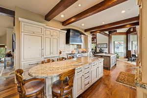 Kitchen featuring a large island, backsplash, dark wood-style floors, beamed ceiling, and light stone counters